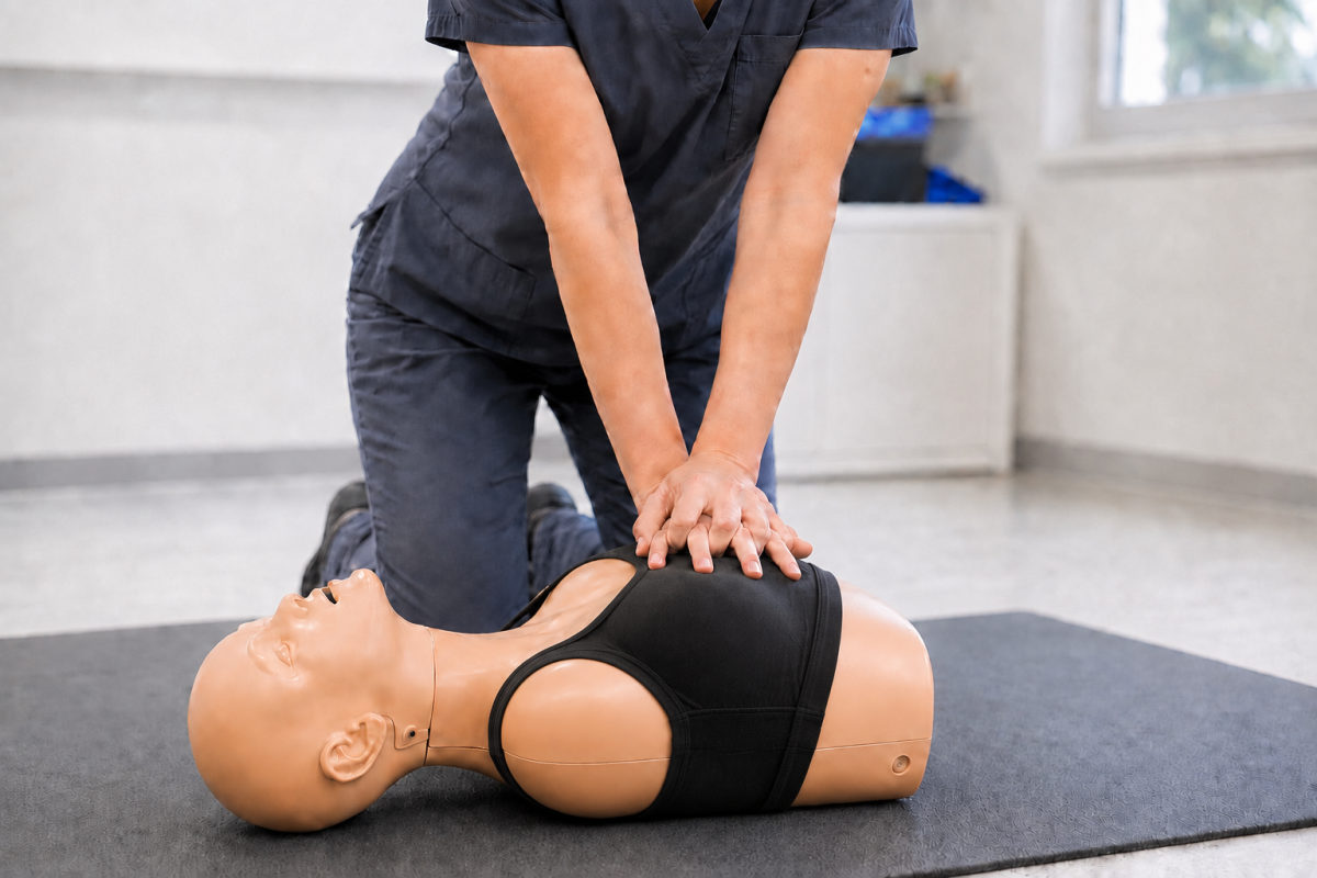 Rescuer performing chest compressions on a female CPR training manikin wearing a black sports bra.
